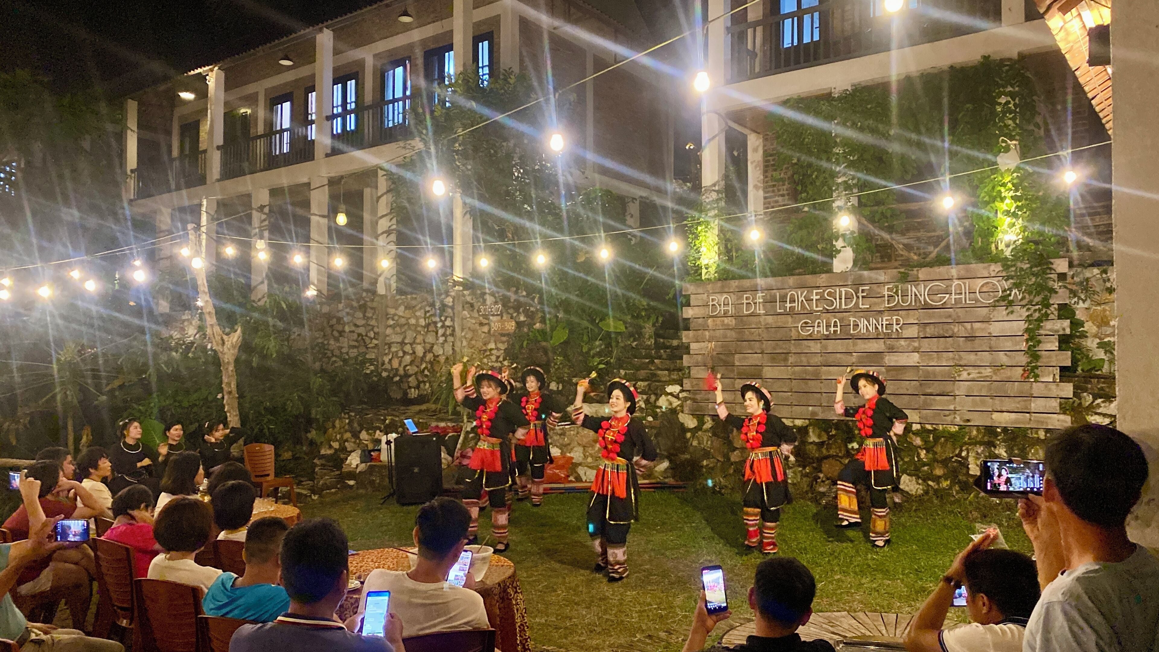 A group of people in traditional attire performing on a stage with a backdrop that reads "BA BE LAKESIDE BUNGALOW GALA DINNER".