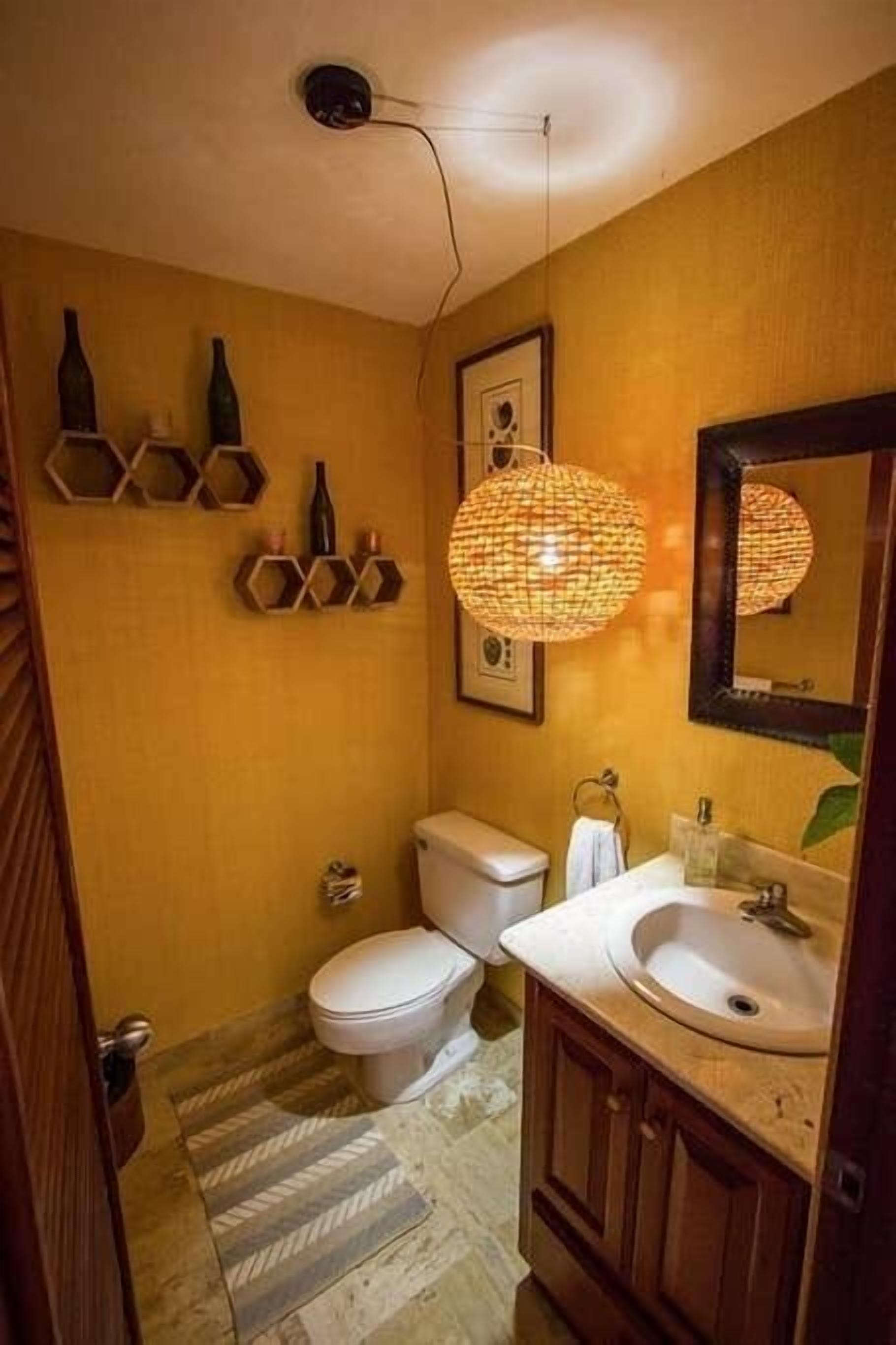 Ein Badezimmer mit Toilette, Waschbecken und Spiegel. Dekorative Wandschränke und eine Pendelleuchte runden den Raum ab.