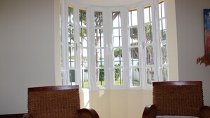 A room with two wooden chairs with white cushions, a large bay window with multiple panes, and a view of greenery outside. - Spacious holiday home by the sea (Chiclana de la Frontera)