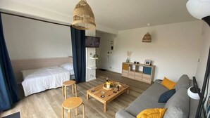 Une pièce moderne et bien éclairée, comprenant un lit, un canapé gris, une table basse en bois et un téléviseur.