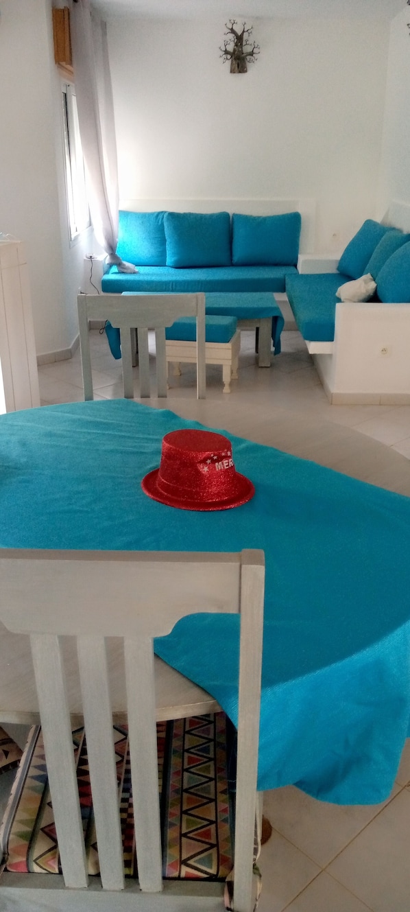 Une pièce comprenant un canapé bleu, une table à manger en bois surmontée d’un napperon rouge et un élément décoratif mural.