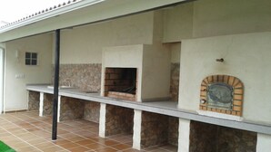 An outdoor kitchen area with a stone wall, a brick oven, and a tiled floor. - Lodging AT-CC-00296,Extremadura,garden,private garage,air conditioning, hydromassage, air conditioning, heating, air conditioner, heating, air conditioner, heating, air conditioner, heating (Zarza de Granadilla)