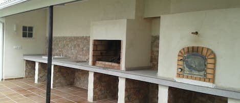 An outdoor kitchen area with a stone wall, a brick oven, and a tiled floor.