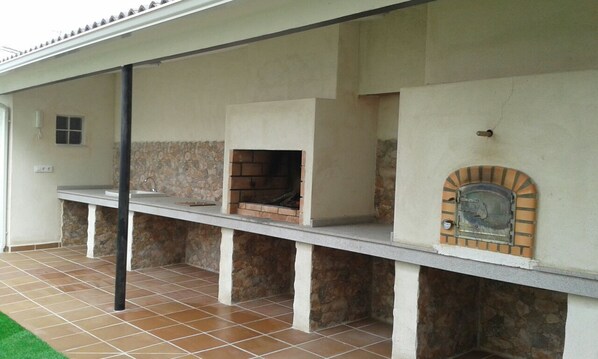 An outdoor kitchen area with a stone wall, a brick oven, and a tiled floor.