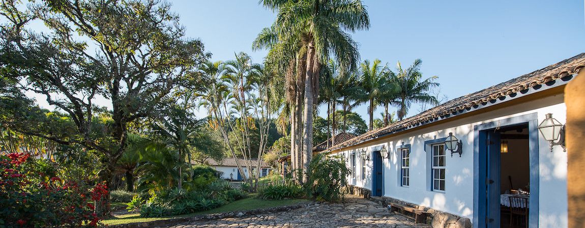 A traditional building with a white facade and blue doors, surrounded by lush greenery and palm trees.