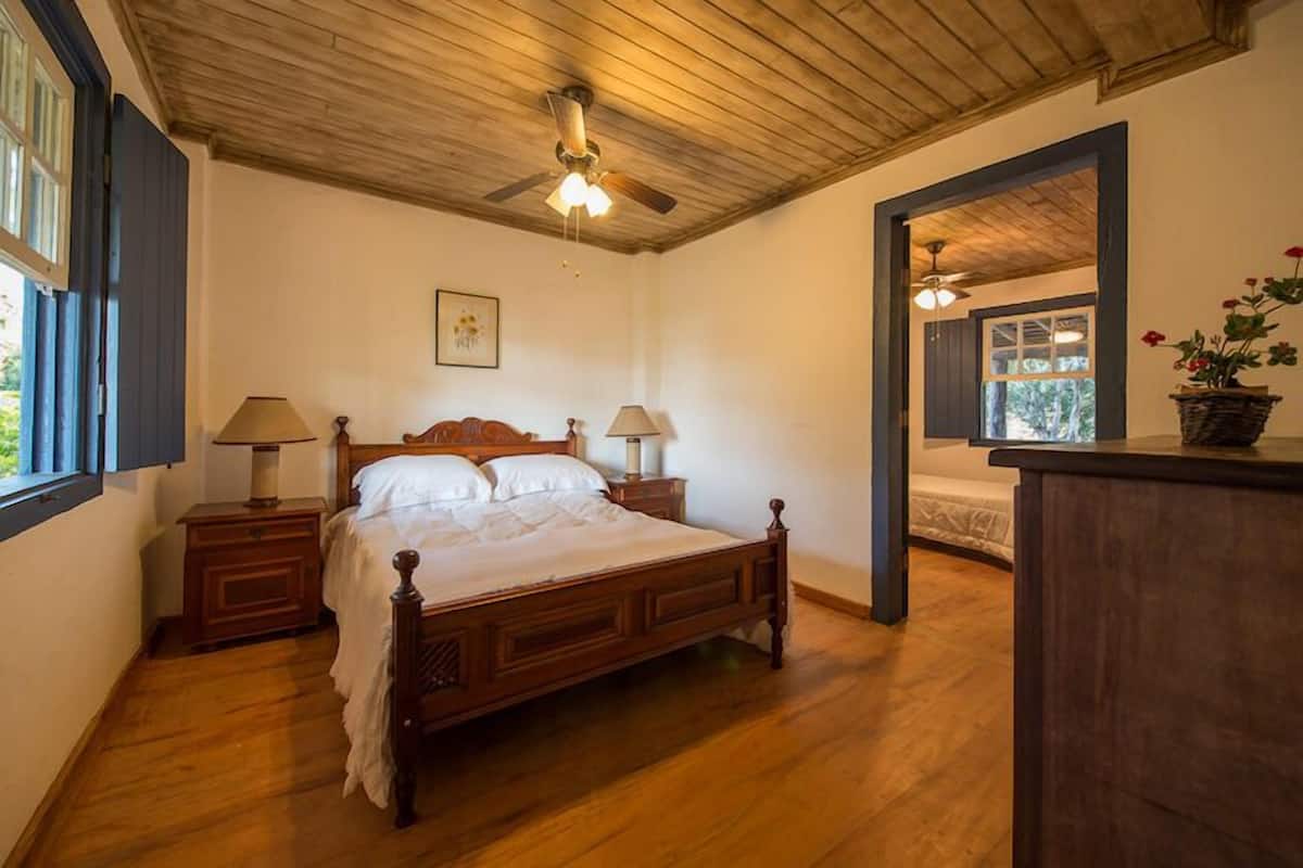 Un dormitorio con una cama de madera, dos mesitas de noche, un ventilador de techo y una ventana.