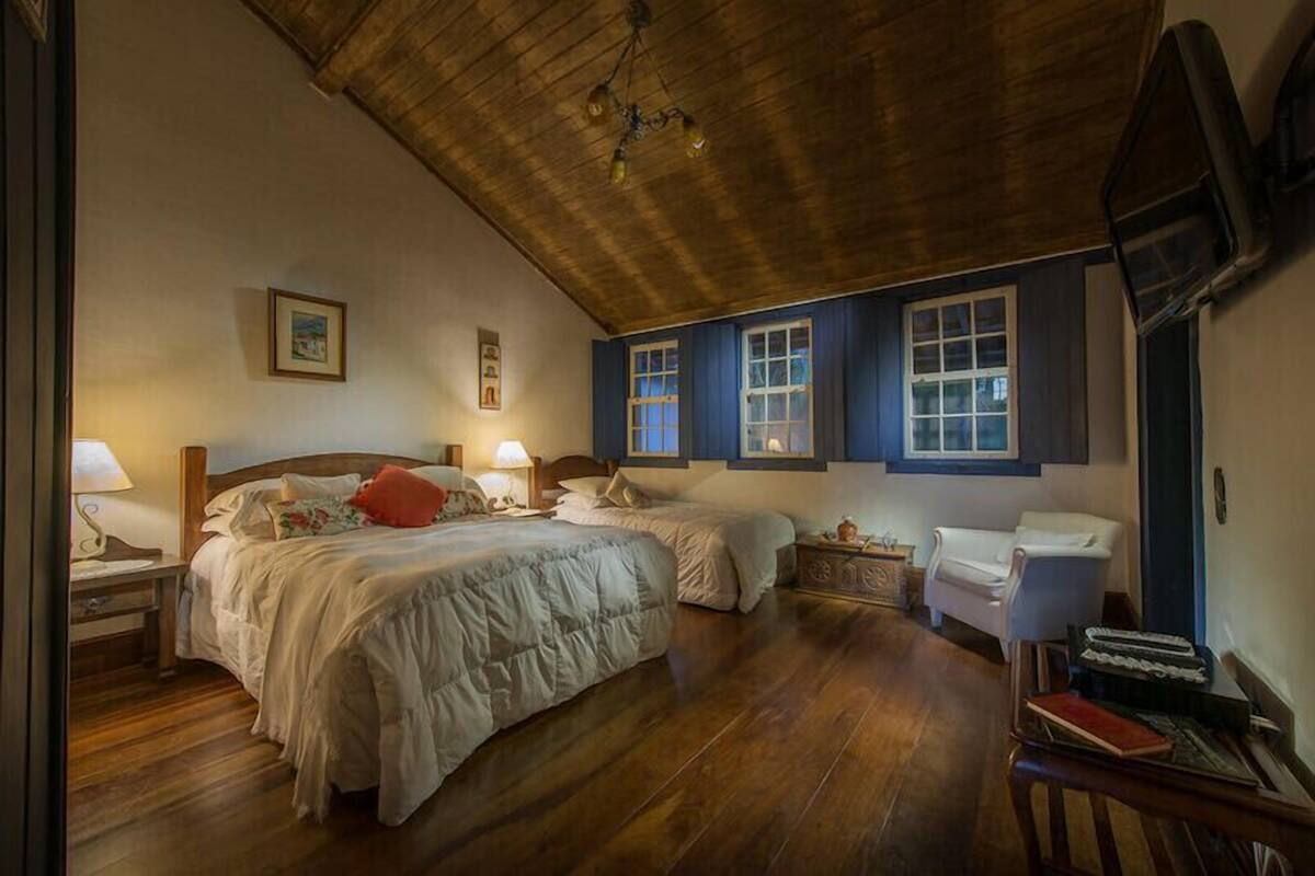 Un dormitorio con dos camas, piso de madera, ventilador de techo y televisor montado en la pared.