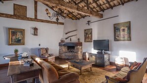 Uma sala de estar rústica com lareira de pedra, sofás de couro, mesa de centro de madeira e uma televisão.