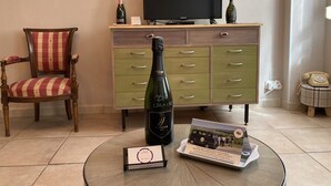 Een woonkamer met een televisie, een fles champagne, een stoel, een kast en een bijzettafeltje met een brochure.