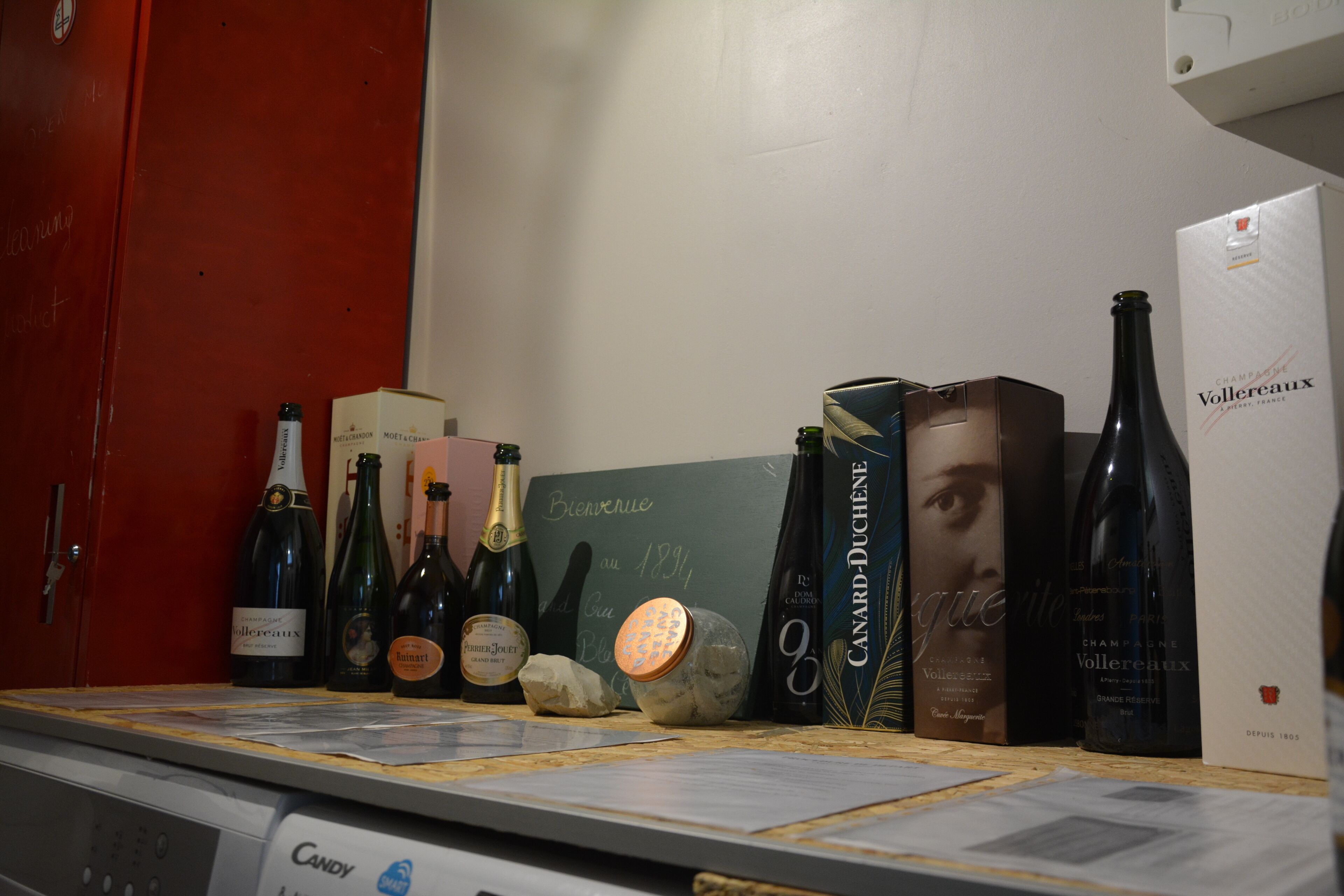 Une présentation de vins comprenant différentes bouteilles et caisses, ainsi qu’un panneau d’affichage en ardoise.