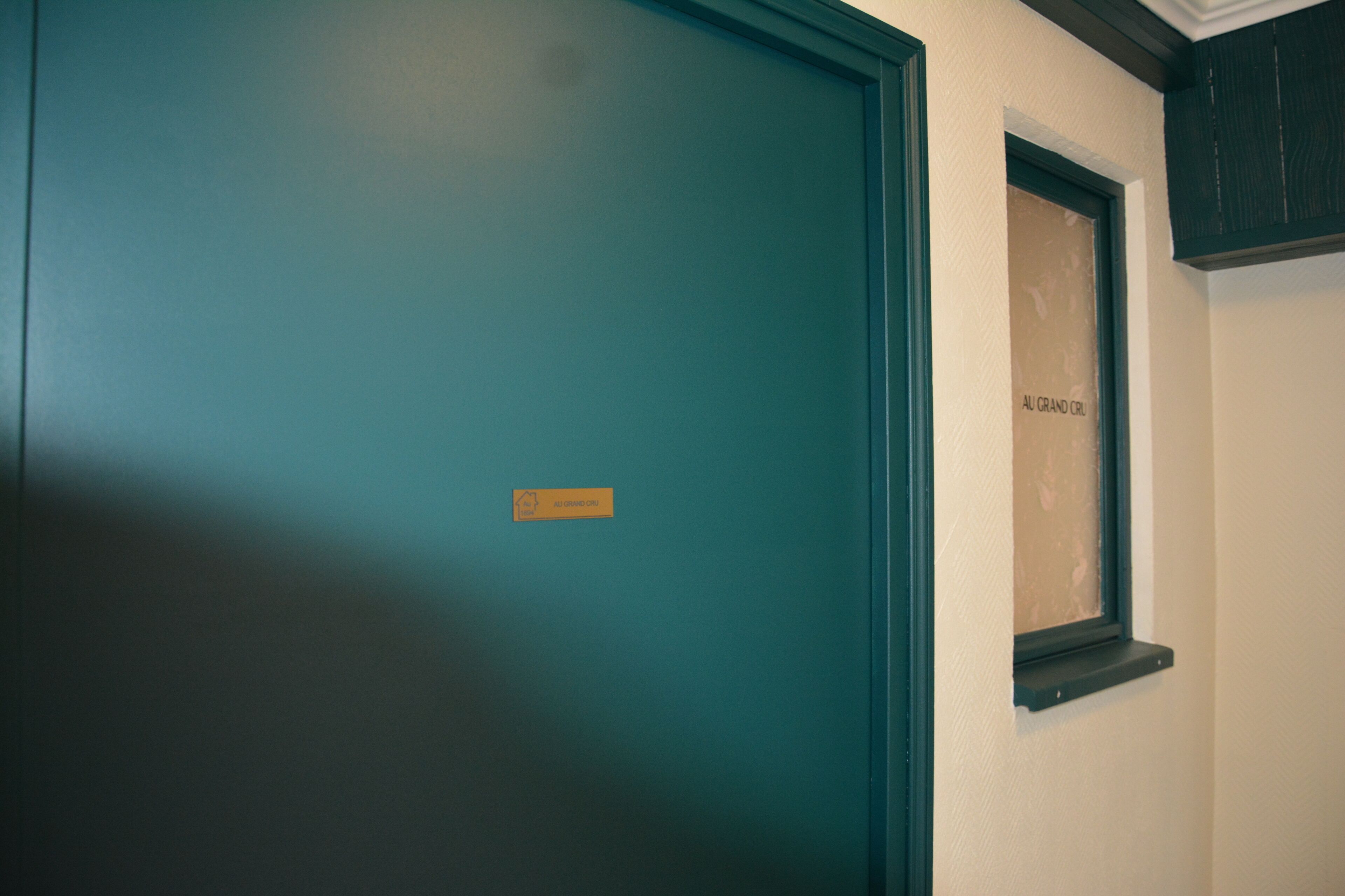 Una puerta azul verdosa con un letrero pequeño, una ventana con una placa y un marco oscuro.