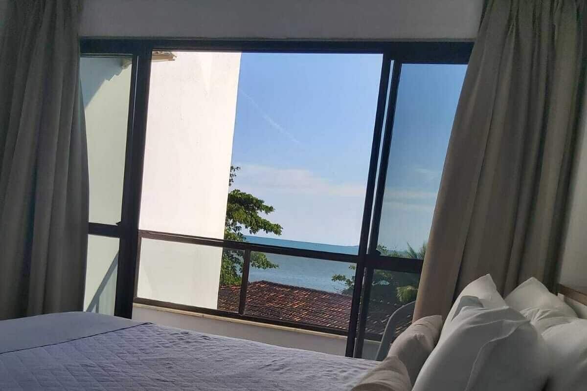 A hotel room with a large bed, a view of the sea, and a balcony with a railing.