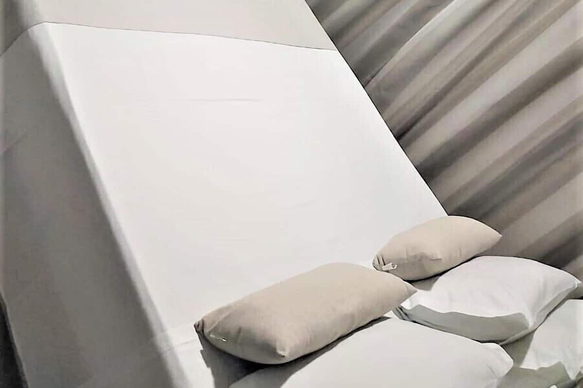 A modern hotel room with a bed, pillows, a window, and curtains.
