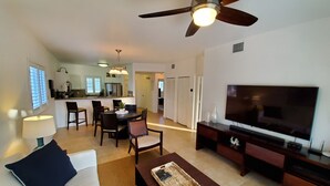 A living room with a sofa, a coffee table, a TV, and a ceiling fan. There is a dining area with chairs and a table in the background. - "Luxurious Villa" 2 Bedroom / 2 Bath (Bimini)