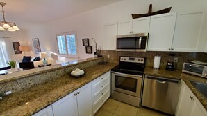 A modern kitchen with white cabinets, stainless steel appliances, granite countertops, and a window providing natural light. - "Luxurious Villa" 2 Bedroom / 2 Bath (Bimini)