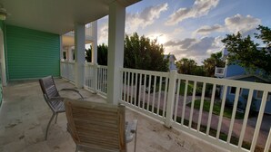 A covered porch with two wooden benches, a white railing, and a view of a residential street with houses and trees. - "Luxurious Villa" 2 Bedroom / 2 Bath (Bimini)