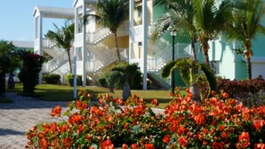 A resort with a white and green building, palm trees, and red flowers in the foreground. - "Luxurious Villa" 2 Bedroom / 2 Bath (Bimini)