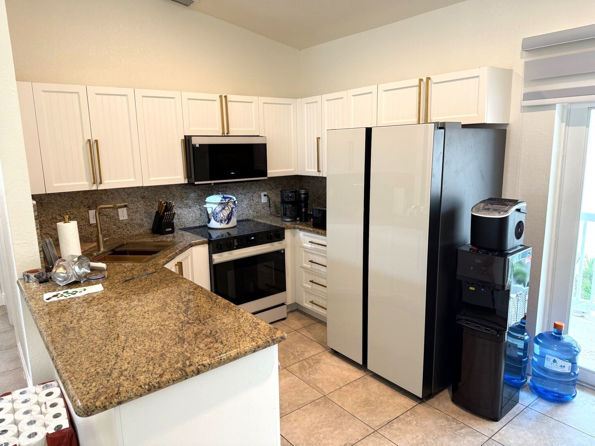 Una cocina moderna con armarios blancos, encimera de granito, refrigerador negro, microondas y cafetera.