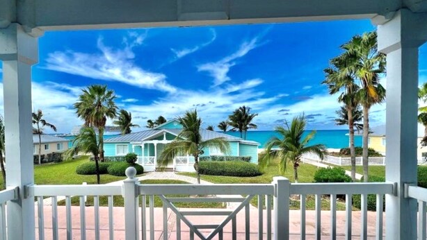 A covered outdoor area with a view of a turquoise building and palm trees, leading to a beach. - Best of Bimini - Oceanview - 2 Bedroom / 2 Bath (Bimini)