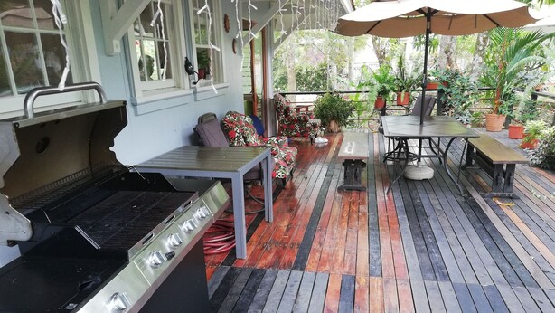 Een terras buiten met een barbecue, houten vloeren en potplanten.