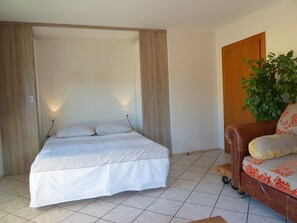 A bedroom with a bed, a wooden wardrobe, a brown sofa with floral cushions, and a potted plant.