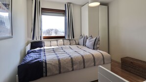 Un dormitorio con cama, cortinas, ventana, mesita de noche y lámpara colgante.