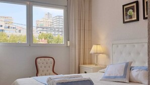 Ein Hotelzimmer mit Bett, Stuhl, Nachttisch und Fenster mit Blick auf Gebäude.