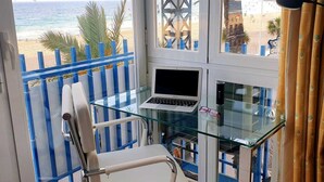 Ein Balkon mit einem Glastisch, einem weißen Bürostuhl und einem Laptop.