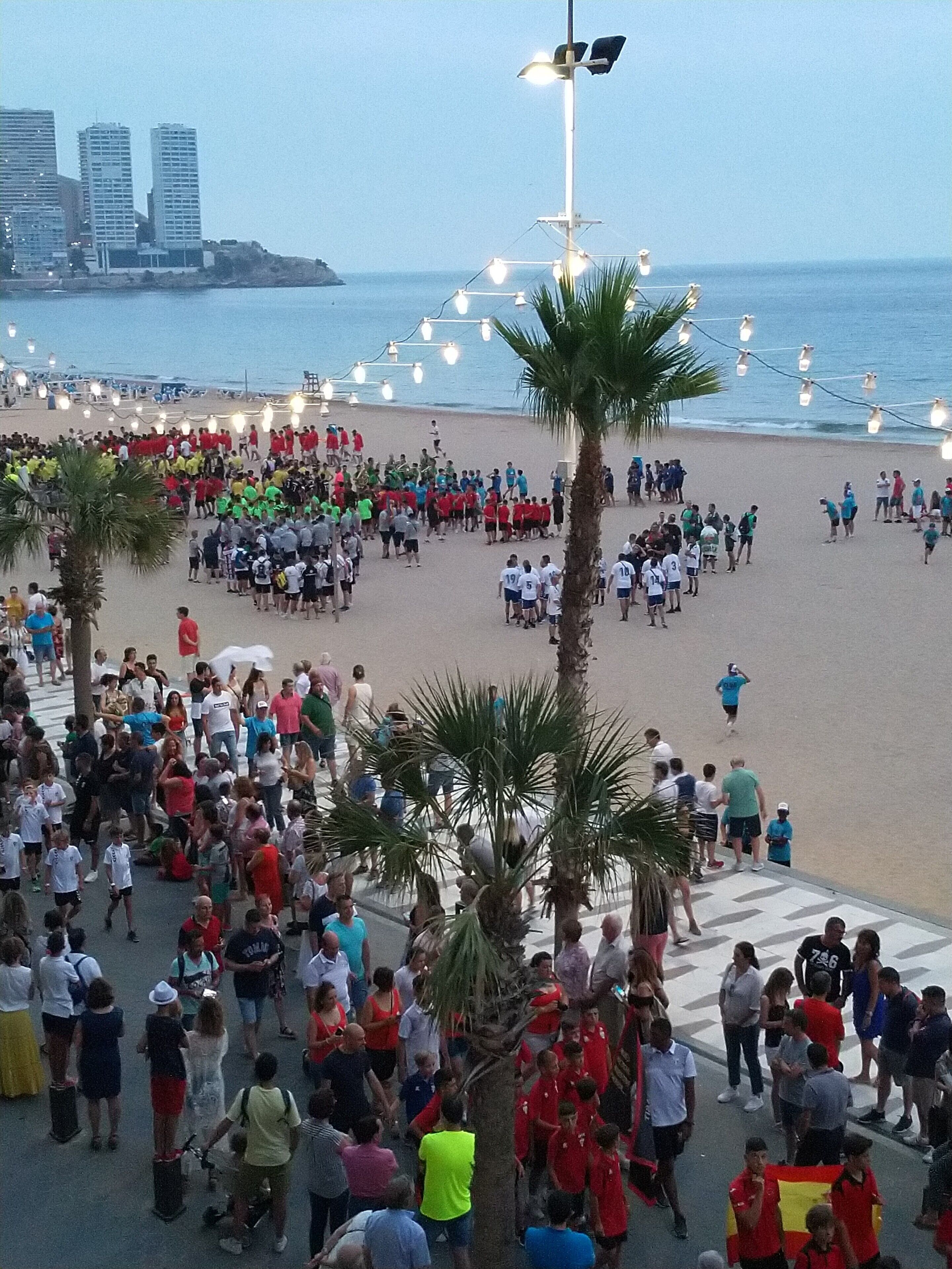 Une plage bondée, bordée de palmiers et éclairée par des lampadaires.
