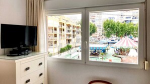Ein Zimmer mit Fernseher auf einem Schrank, einem Sessel und einem Fenster mit Blick auf Gebäude und eine Straße.