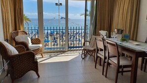 Ein Balkon mit Blick auf den Strand, Korbmöbel und ein Esstisch mit Gläsern und einer Obstschale.
