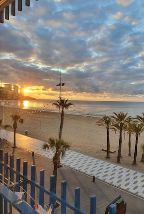 Vista da praia com palmeiras, uma passarela e um pôr do sol.