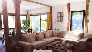 Un salon spacieux avec un grand canapé d’angle beige, une table basse en bois et une vue sur l’extérieur grâce à de grandes fenêtres.