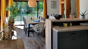 Une cuisine moderne avec un îlot central en bois, un coin repas avec des chaises et une grande fenêtre donnant sur un paysage verdoyant.