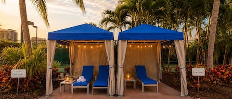 A covered outdoor seating area with two lounge chairs, a small table with a lantern, and a sign indicating 'Private Cabana 1'.