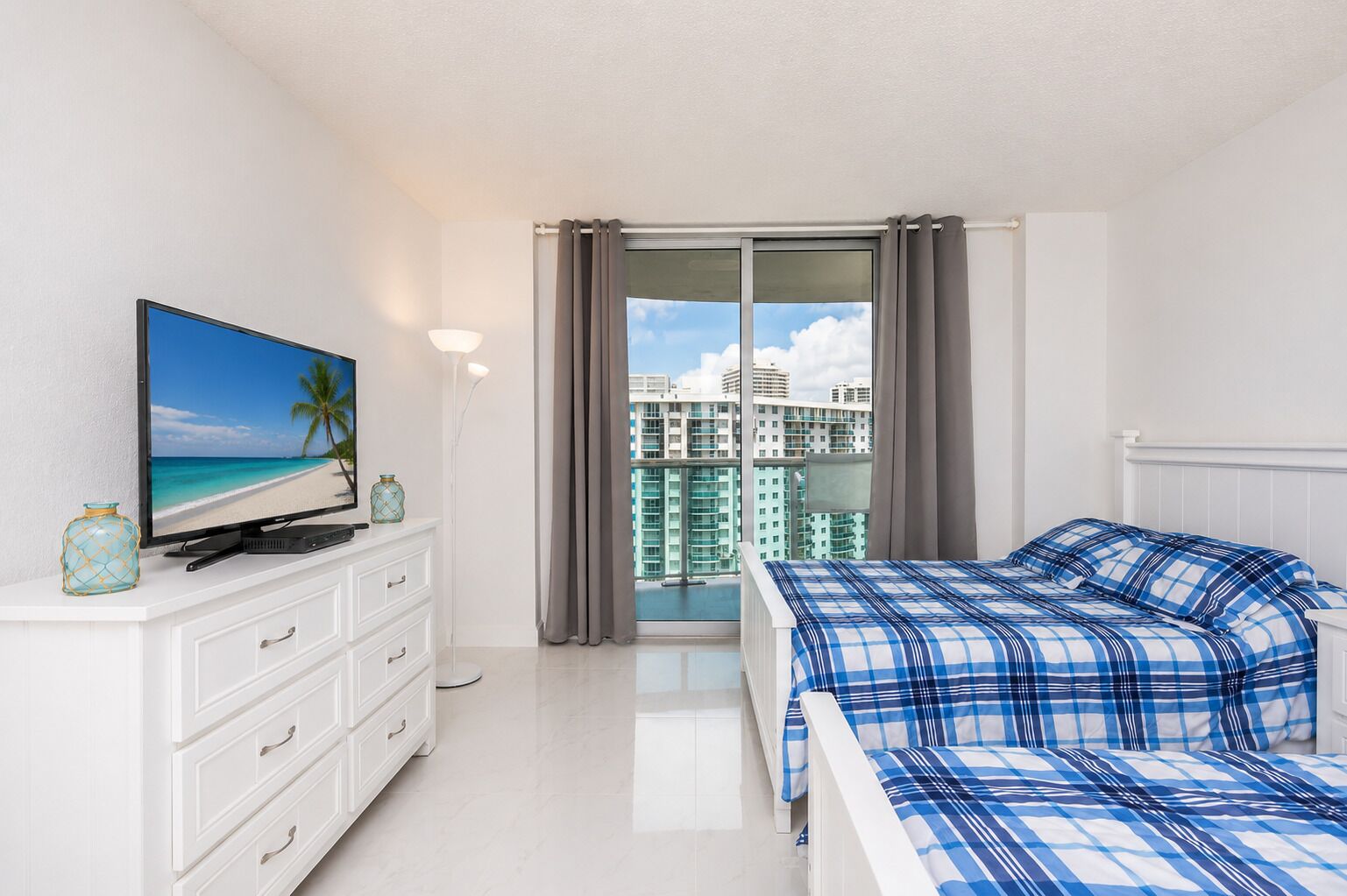 Une chambre d’hôtel avec un lit, un téléviseur posé sur une commode, une vue sur le paysage urbain et un balcon avec des rideaux.