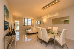 A modern living room with a glass dining table, white sofas, and a city view.