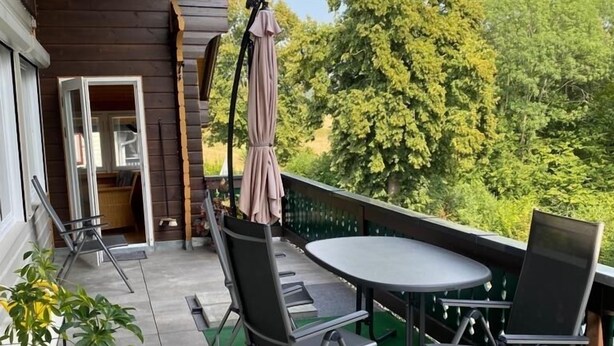 A covered outdoor patio with a round table and four chairs, a potted plant, and a view of trees and sky. - Welcome to the "Hohe Liebe" vacation apartment (Bad Schandau-Ostrau)