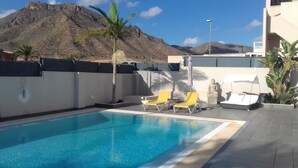 Ein Swimmingpool mit zwei gelben Liegestühlen und einer Buddha-Statue.