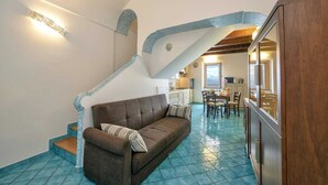 Un vaste espace de vie avec un canapé marron, un escalier agrémenté de touches de bleu et une cuisine en arrière-plan.