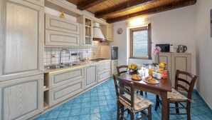 Une cuisine avec des meubles de rangement en bois, une table à manger avec des chaises, une fenêtre donnant sur un beau paysage et une horloge au mur.