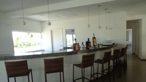A kitchen with a bar area, bar stools, hanging pendant lights, and a view of the outdoors. - Hotel Abrolhos (Nova Viçosa)