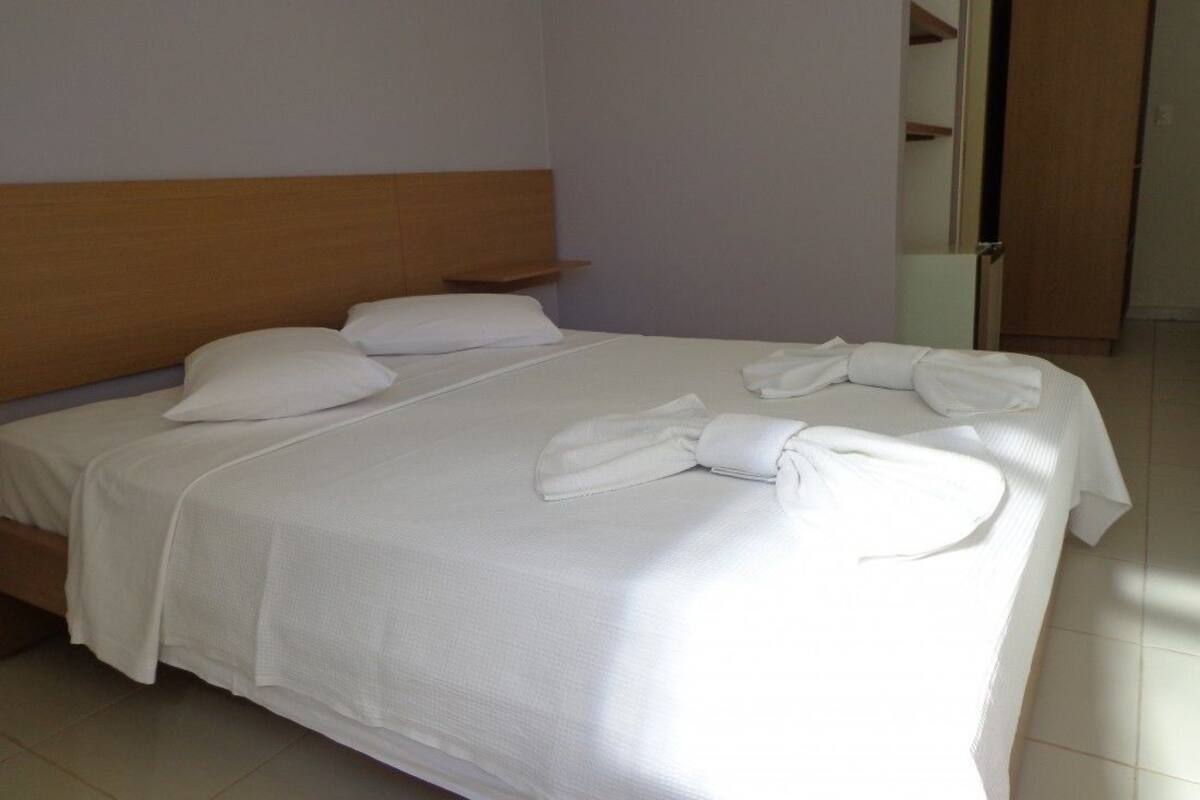 Ein ordentlich bezogenes Bett mit weißen Leinen und Handtüchern, ein Holz-Kopfbrett und ein Fliesenboden.