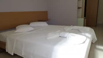 A neatly made bed with white linens and towels, a wooden headboard, and a tiled floor.