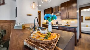 A modern kitchen with wooden cabinetry, a central island with a fruit platter, hanging pendant lights, and a vase with blue flowers.