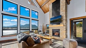 A spacious living room with large windows, a fireplace, and a view of a lake and mountains.