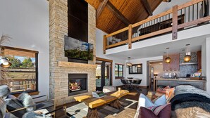 A spacious living area with a stone fireplace, a dining table, and a high ceiling with exposed beams.