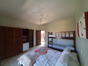 Un dormitorio con una cama litera, un armario, un ventilador de techo y una cama con colcha estampada.
