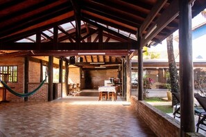 Un patio descubierto y techado con suelo de ladrillo, vigas de madera y una mesa dispuesta para comer.