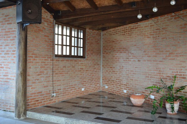 Una habitación con paredes de ladrillo, techo de vigas de madera, una ventana, suelo de baldosas y una planta en maceta.